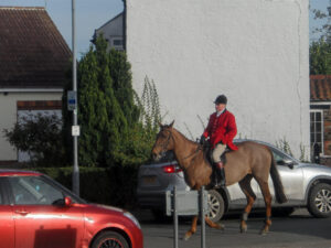 Rider in a red jacket on a horse beside village houses.